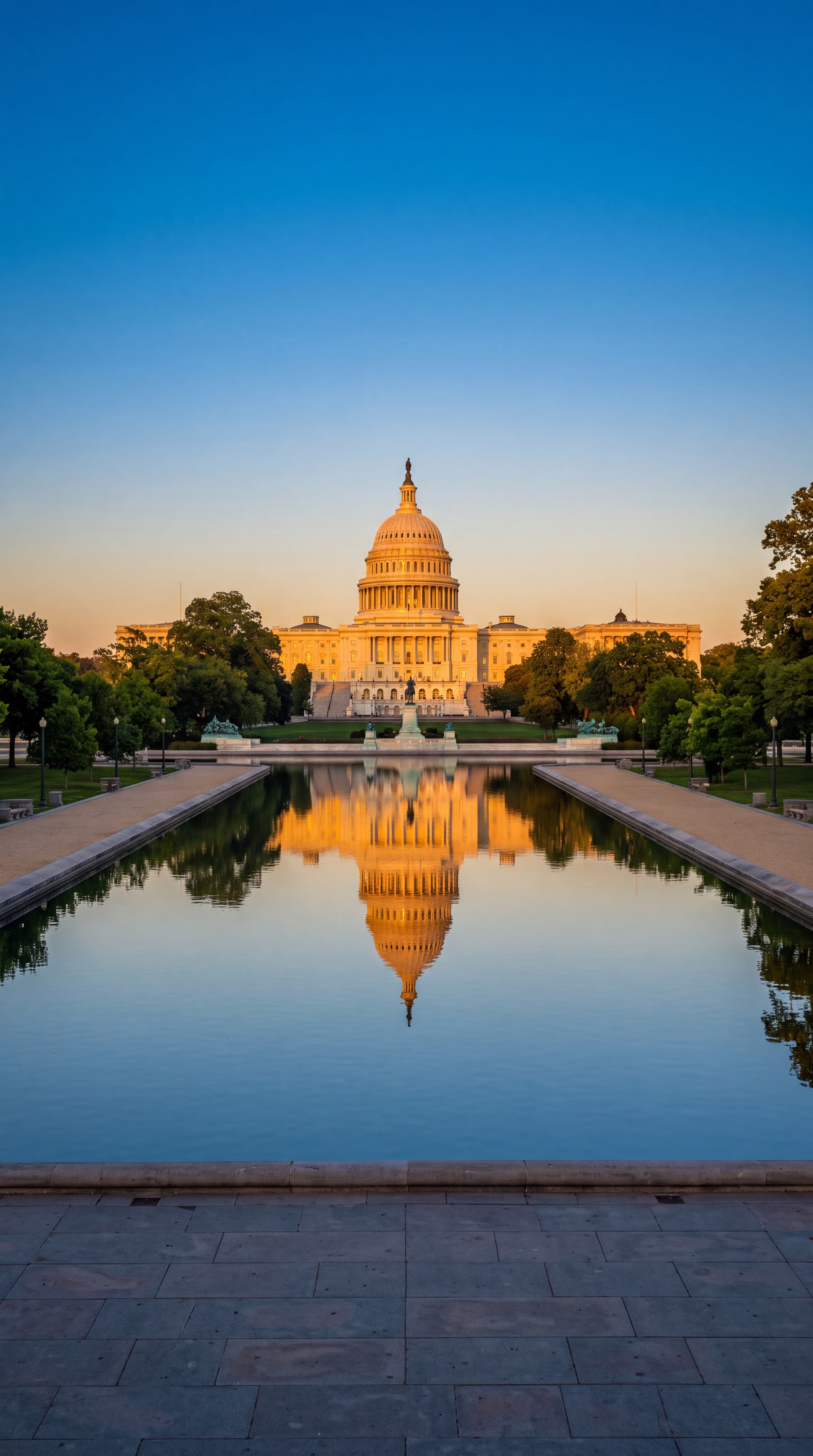 The image shows the United States Capitol building reflected in a calm pool of water during sunset.