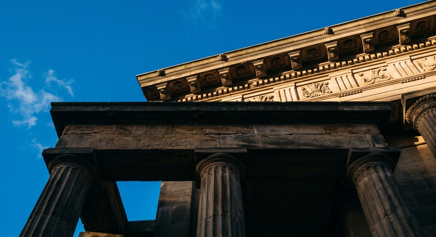 A low-angle view of a classical building with columns and decorative elements against a blue sky.