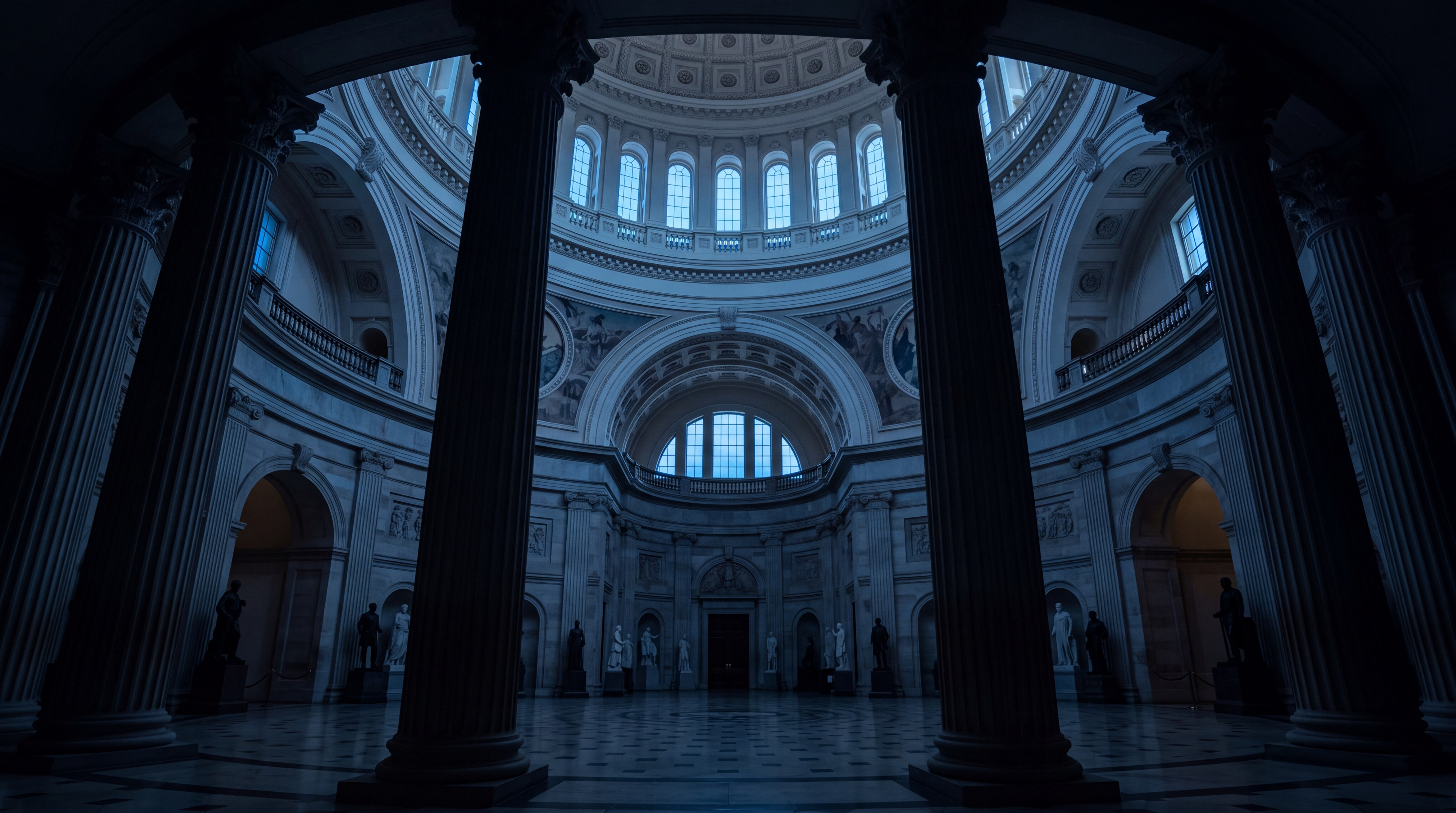 A dimly lit interior of a grand architectural space featuring tall columns and sculptures.