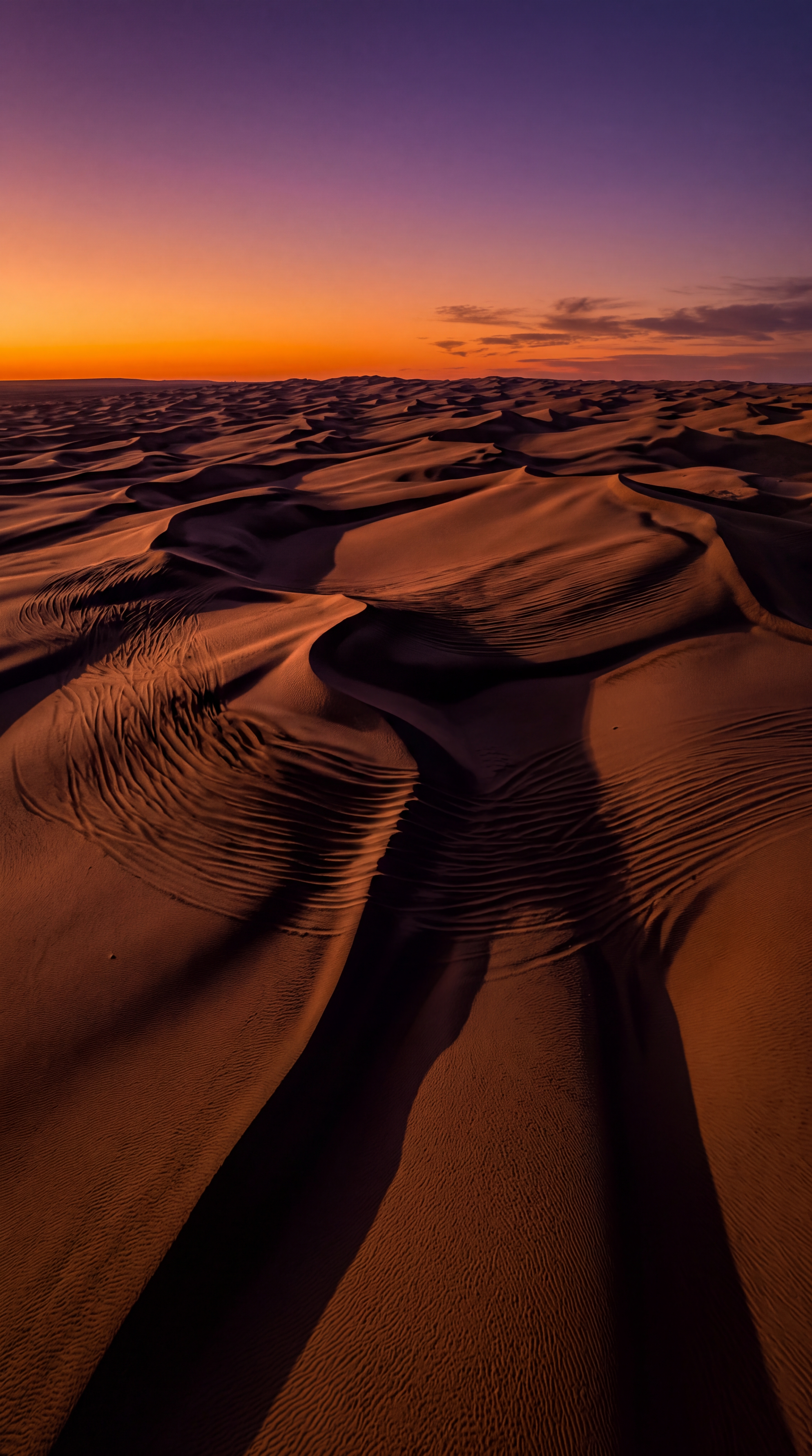 A vast expanse of sand dunes under a colorful sunset.