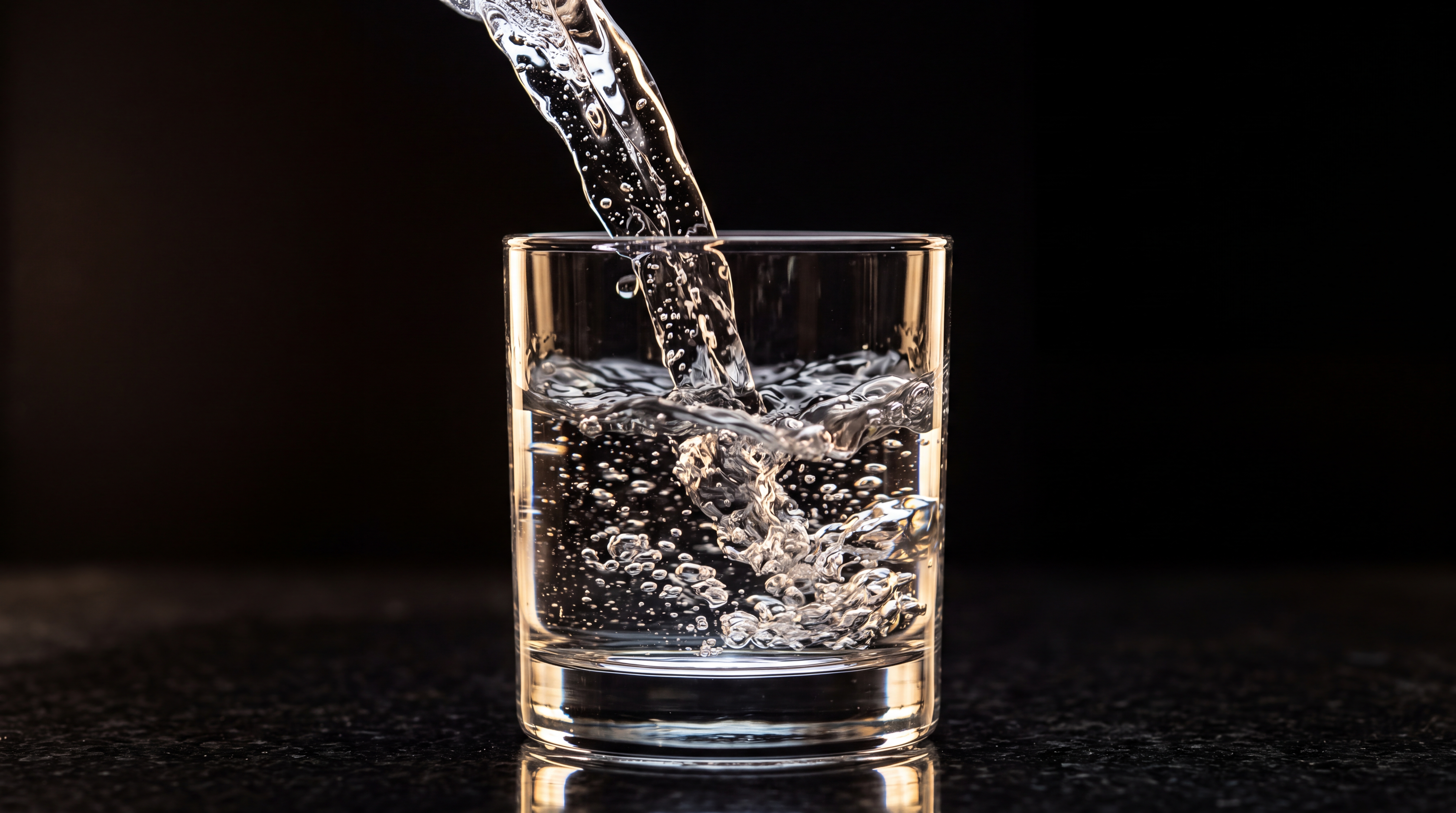 A stream of water is being poured into a clear glass filled with bubbles.