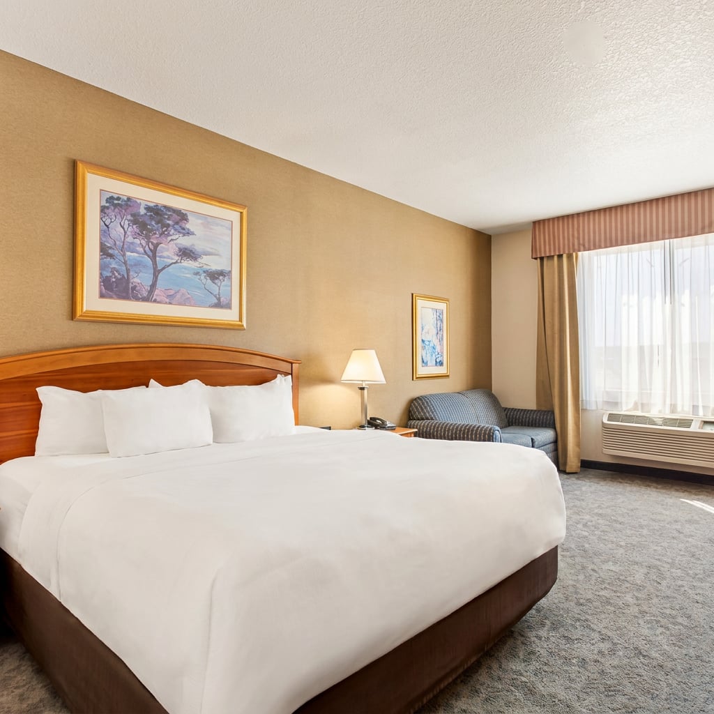A well-furnished hotel room featuring a large bed, a lamp, and a seating area.