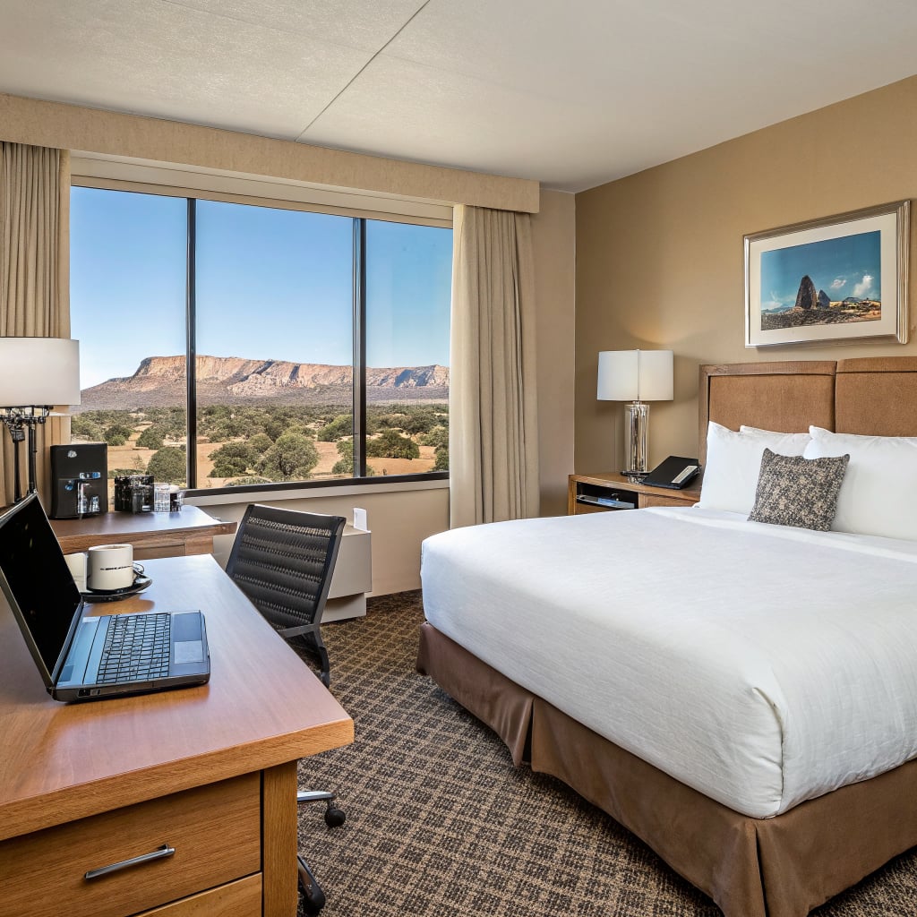 A hotel room featuring a bed, desk, and a large window with a view of a mountainous landscape.