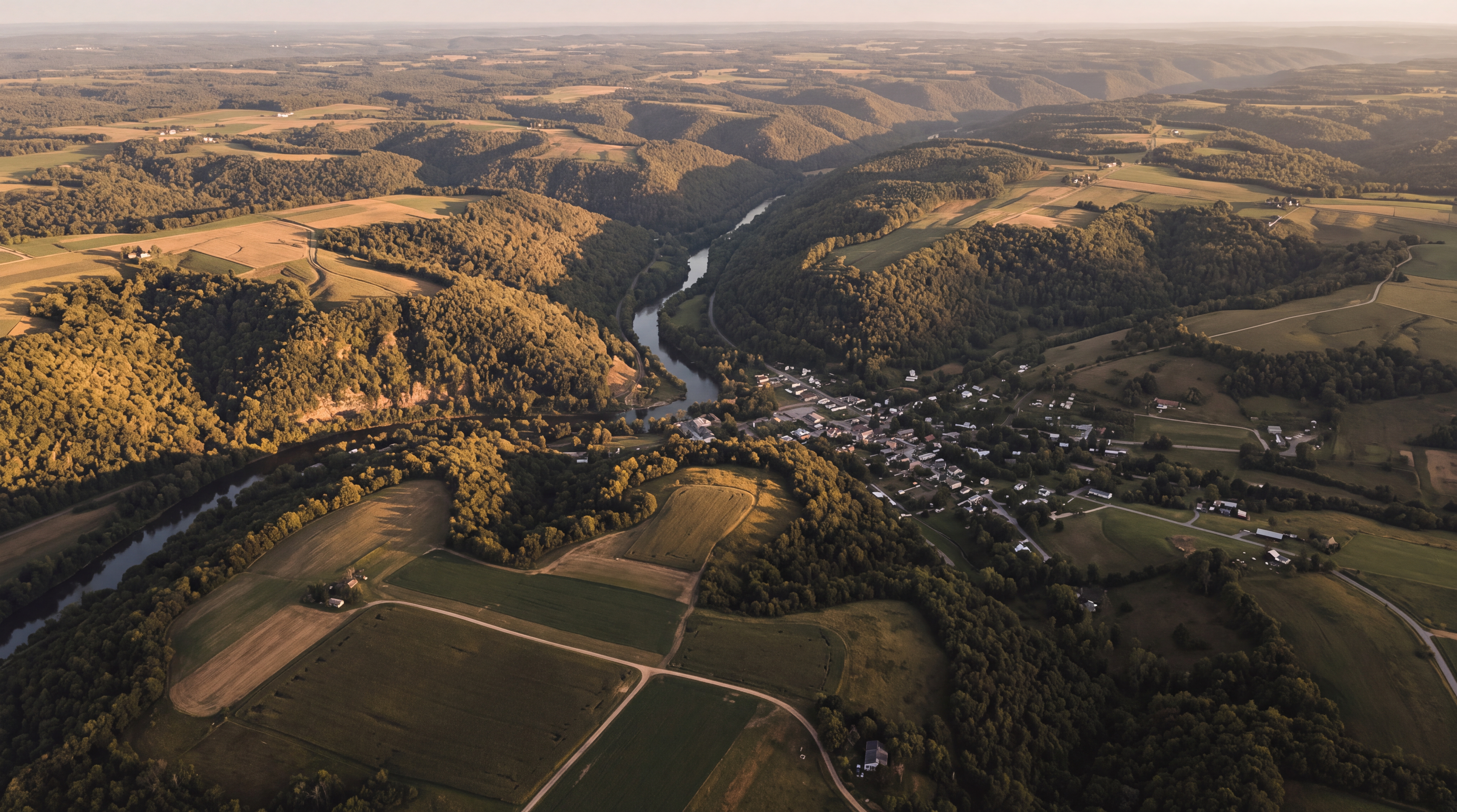 An aerial view of a rural landscape with rolling hills and a river running through a small village.