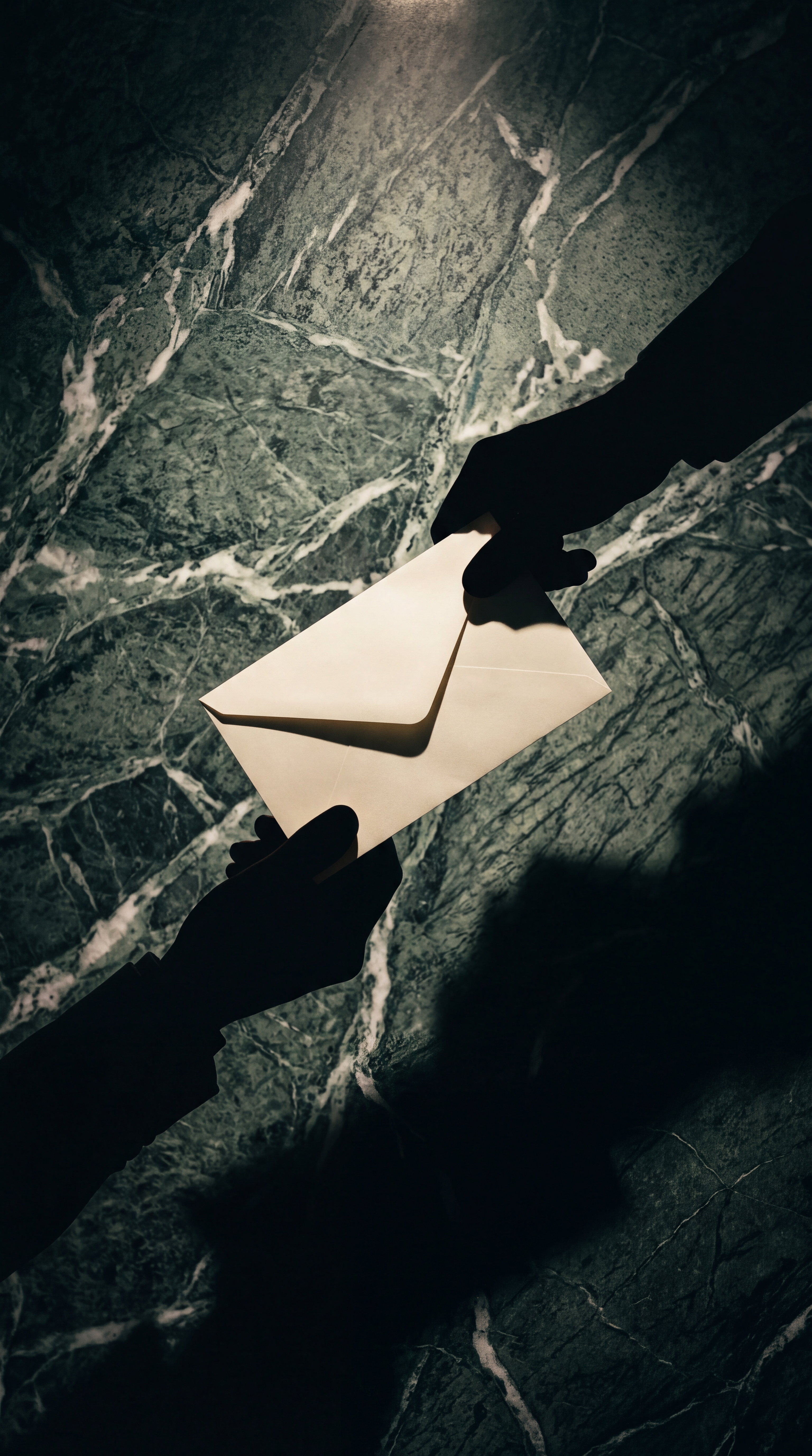 Two hands are exchanging an envelope against a marble background.