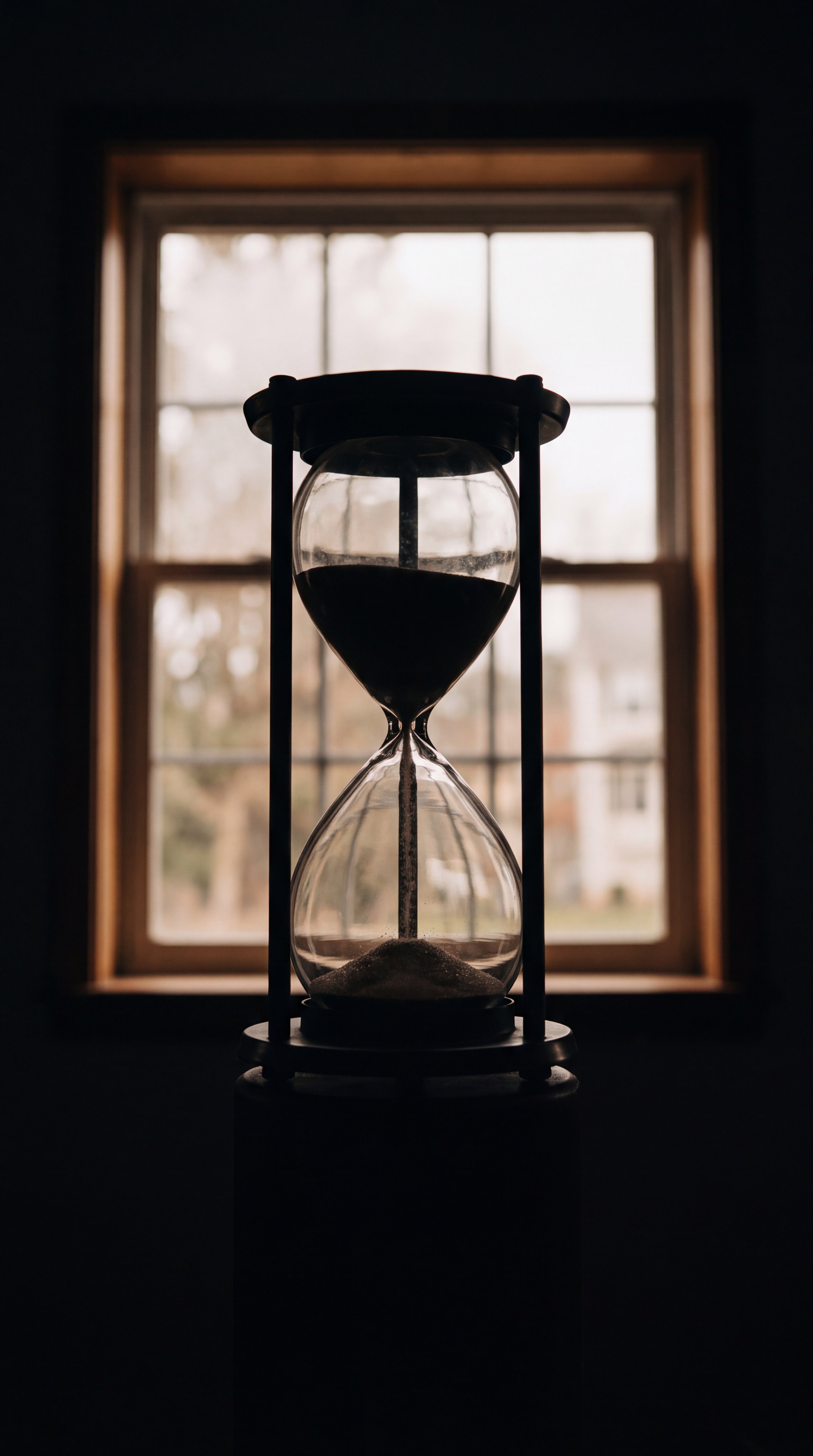 An hourglass is silhouetted against a window.