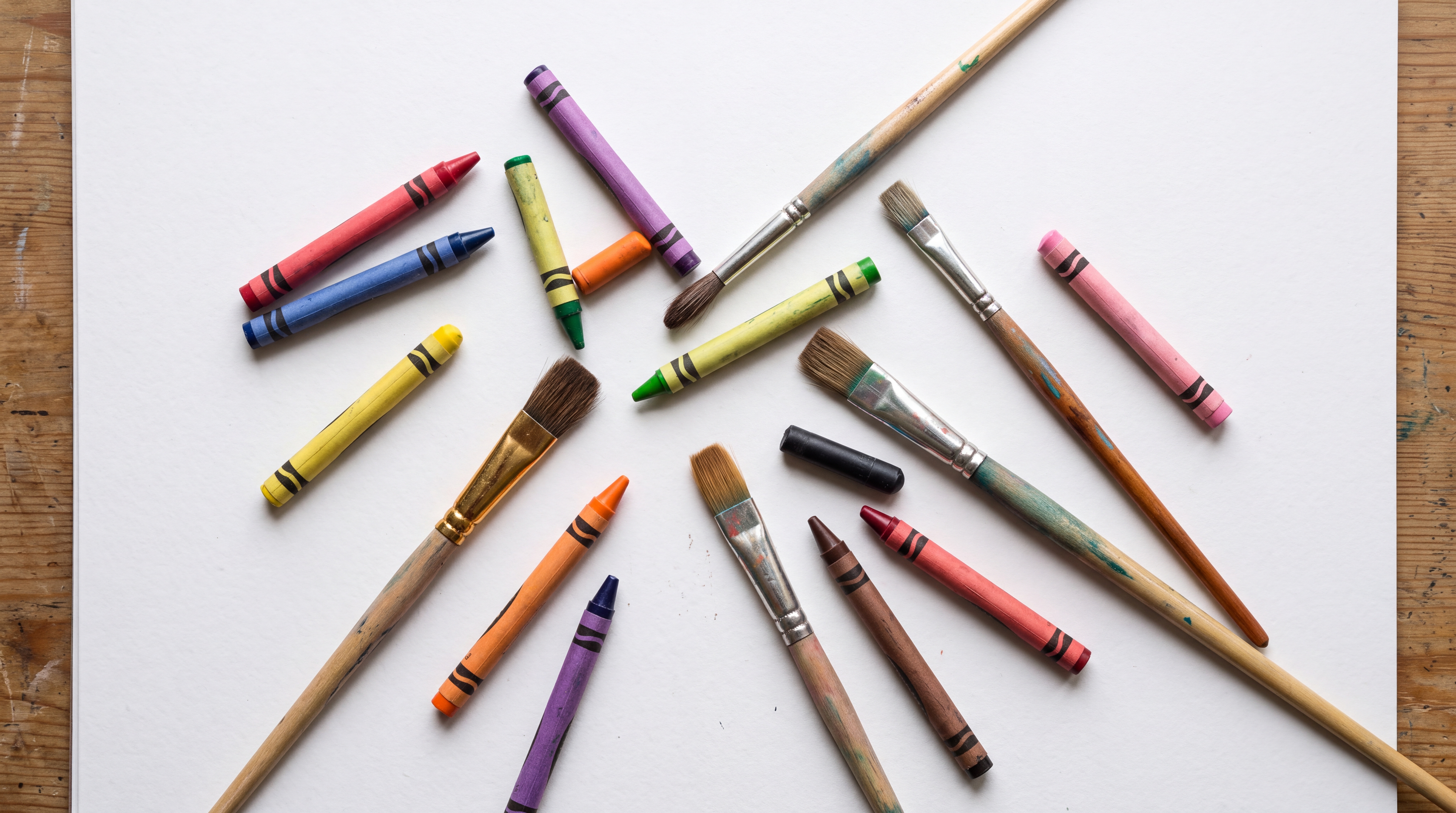A collection of paintbrushes and crayons arranged on a blank sheet of paper.