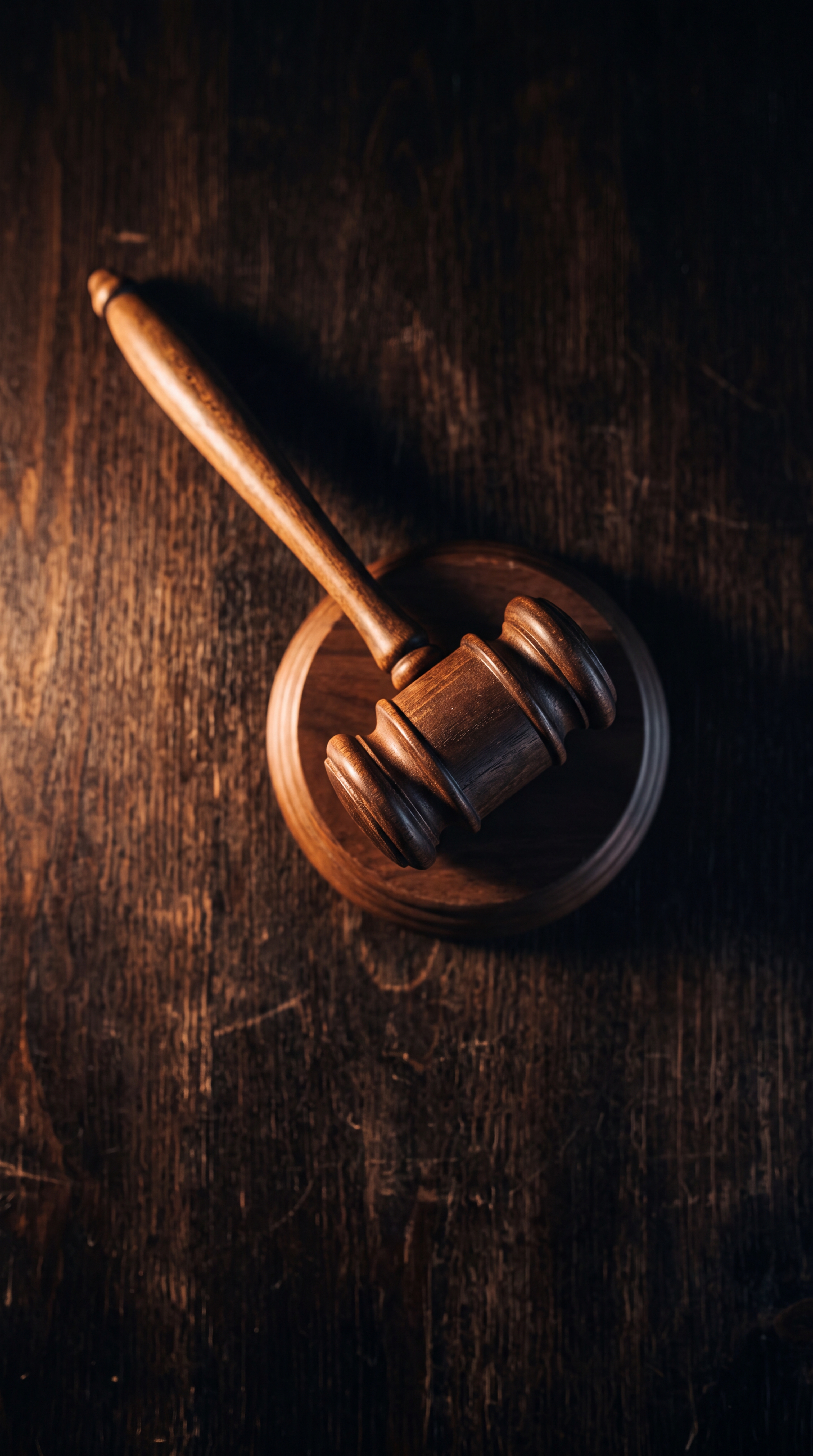 A wooden gavel resting on a circular base on a dark wooden surface.