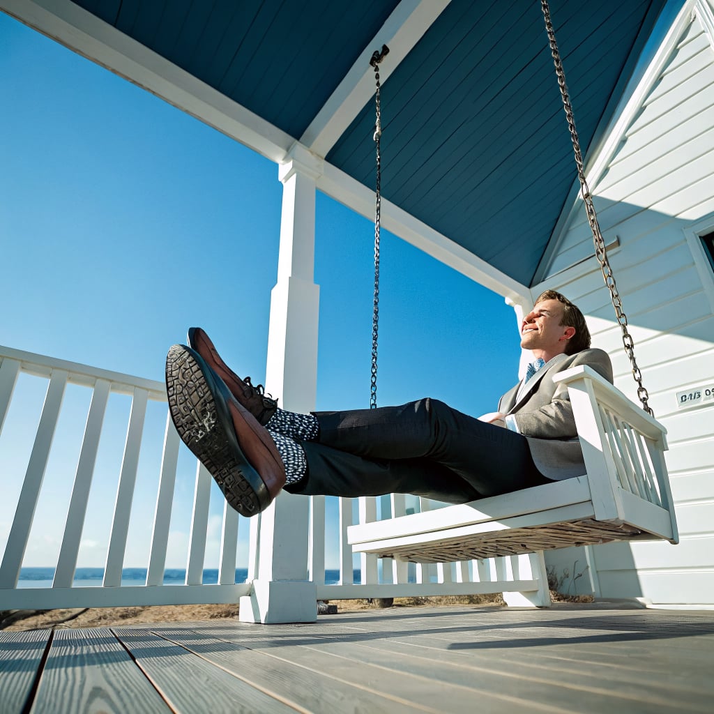 A man in a suit is sitting on a swing on a porch with a clear blue sky in the background.