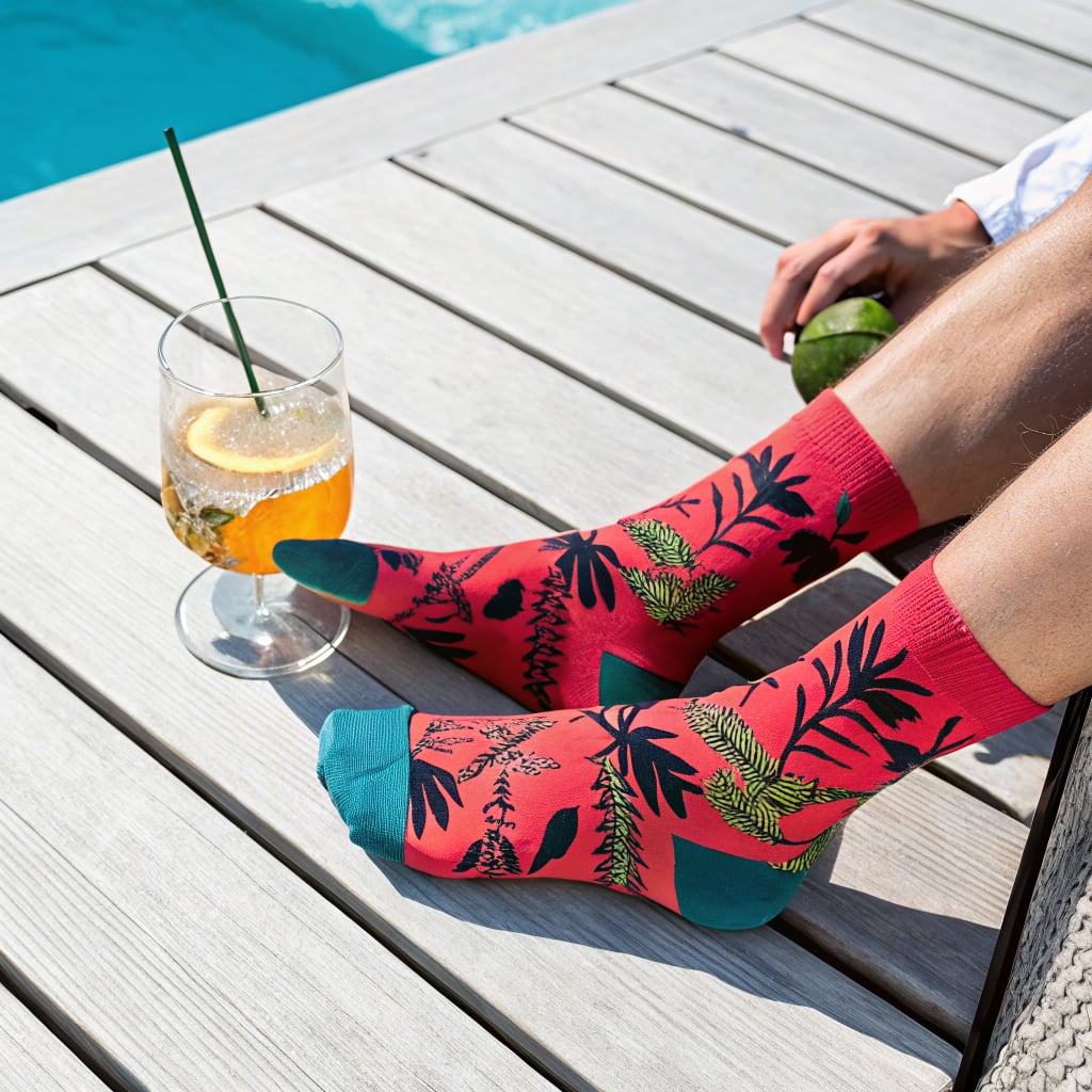 A person sitting by a pool wearing colorful socks and holding a drink.