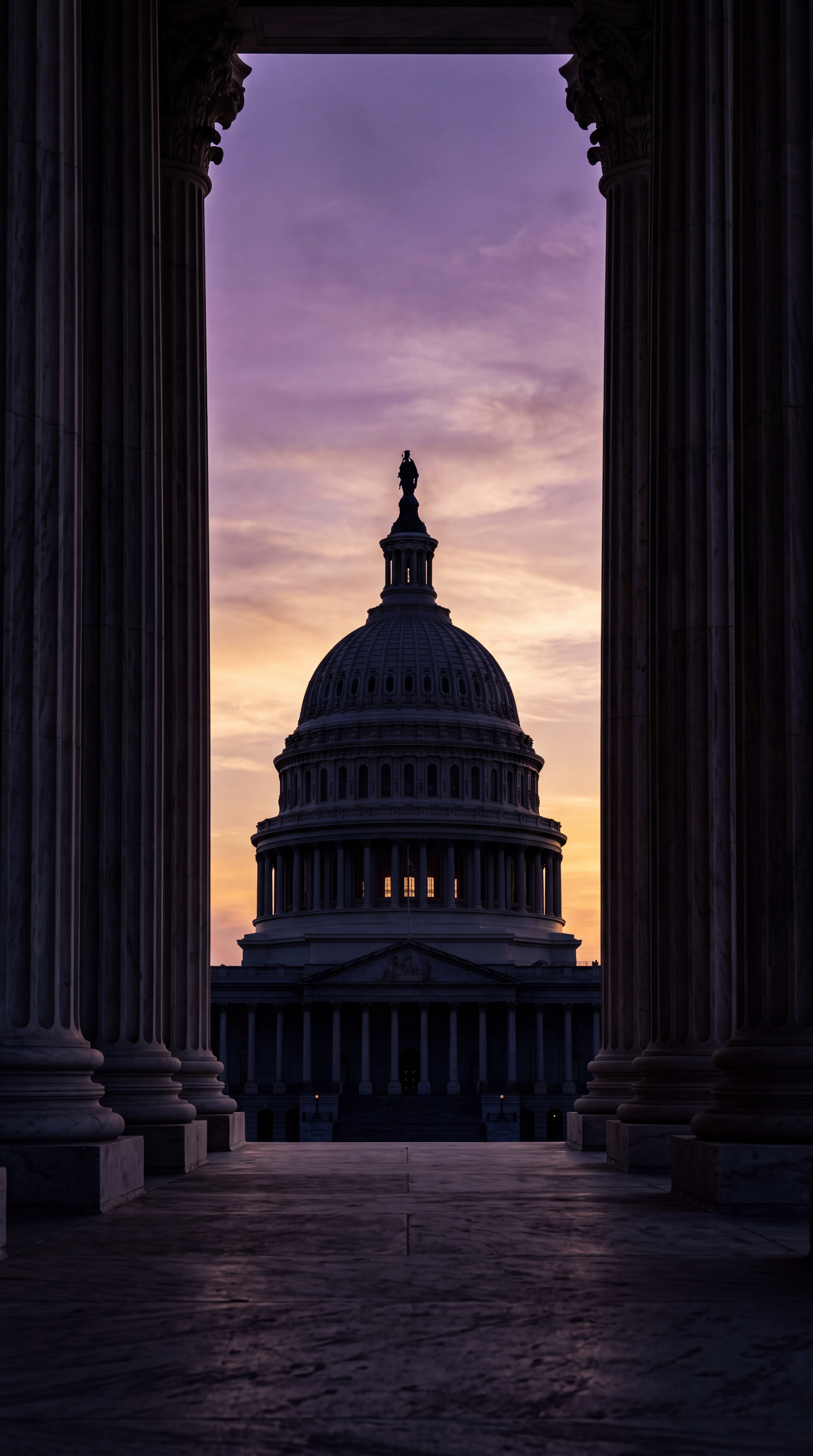 The image shows the silhouette of a dome building framed by columns at sunset.