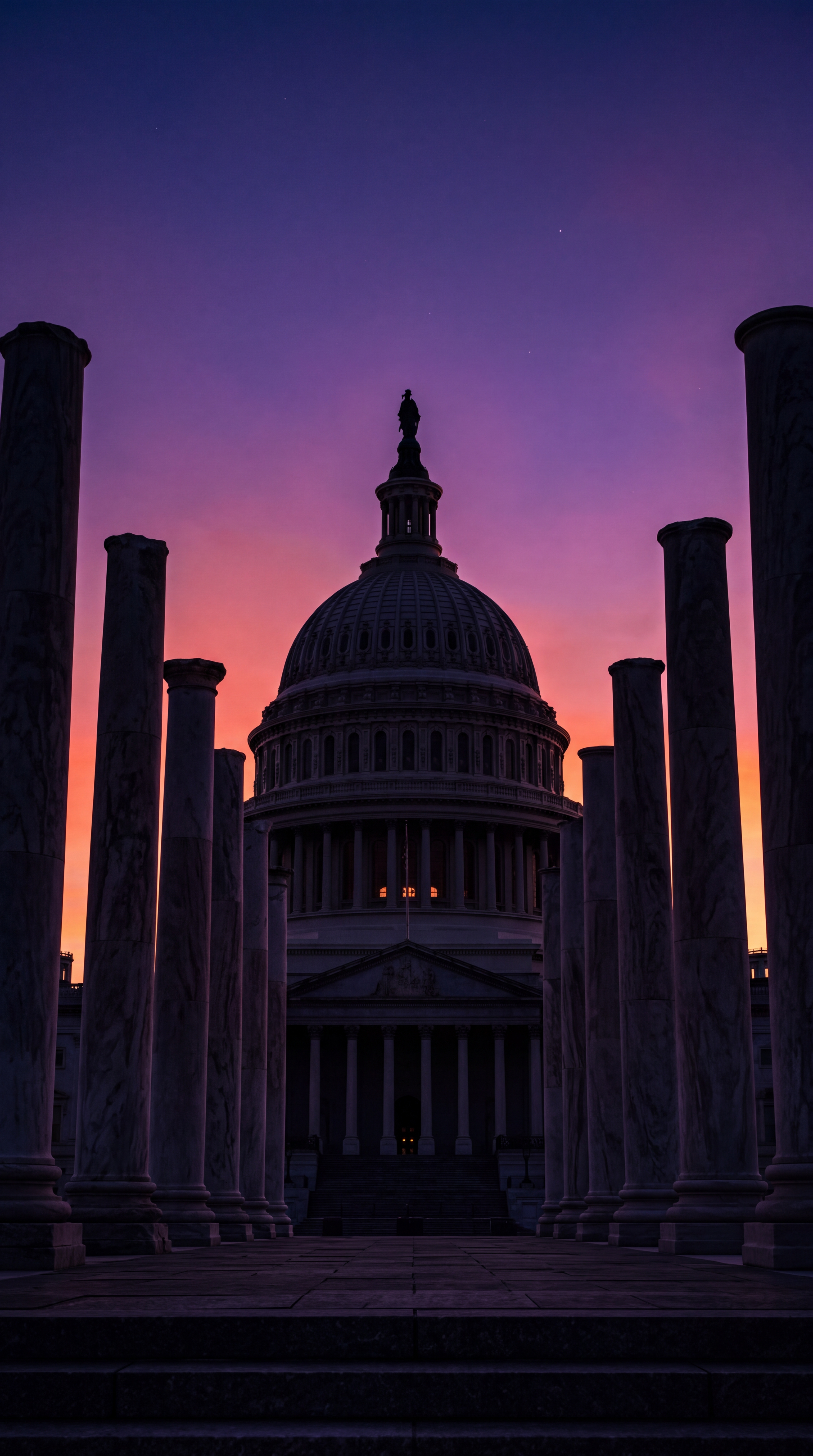 The image shows the silhouette of a large dome building surrounded by columns against a colorful sunset sky.